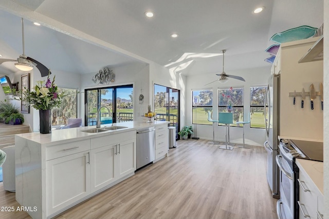 kitchen with sink, stainless steel appliances, light stone counters, white cabinets, and a center island with sink