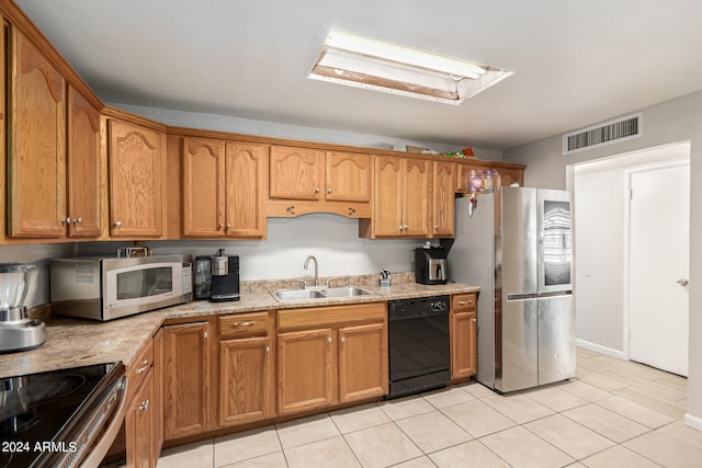 kitchen featuring a skylight, light tile patterned floors, light stone counters, stainless steel appliances, and sink