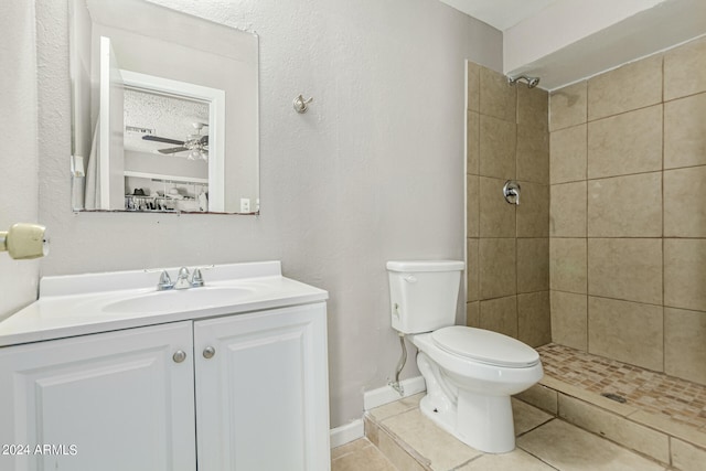 bathroom with tile patterned floors, toilet, a tile shower, ceiling fan, and vanity