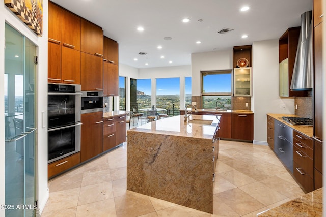 kitchen with appliances with stainless steel finishes, tasteful backsplash, an island with sink, sink, and light stone counters