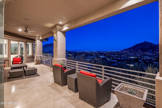 patio at night featuring ceiling fan, a mountain view, and a balcony