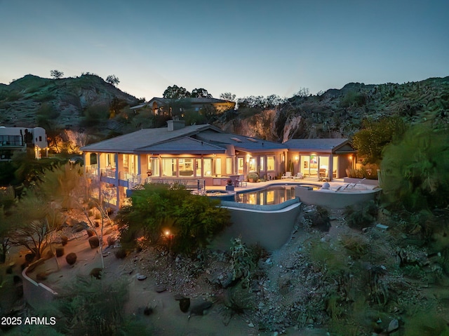 back house at dusk featuring a mountain view and a patio area