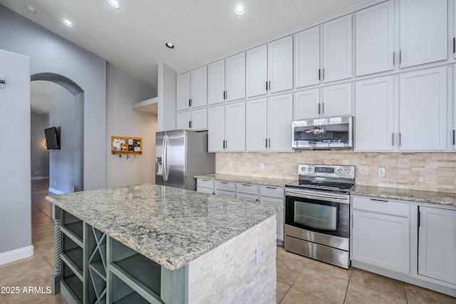 kitchen with light stone counters, white cabinetry, stainless steel appliances, and a kitchen island