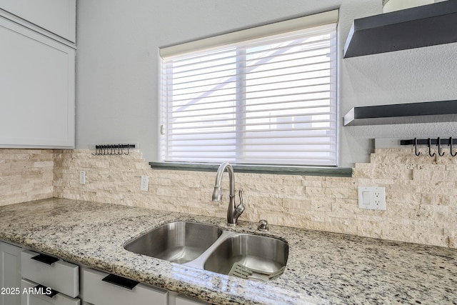 kitchen with sink, decorative backsplash, light stone countertops, and white cabinets