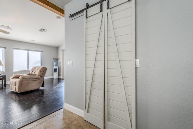 corridor with beamed ceiling, a barn door, and tile patterned floors