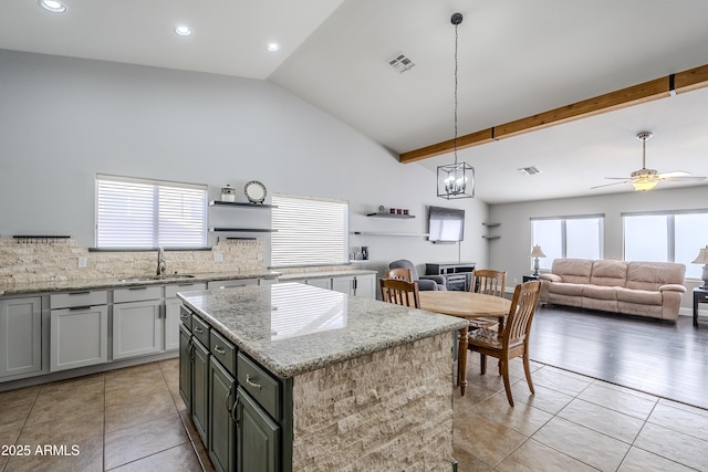 kitchen with sink, vaulted ceiling with beams, backsplash, a center island, and light stone countertops