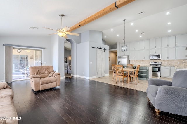 living room featuring sink, vaulted ceiling with beams, hardwood / wood-style flooring, and a barn door