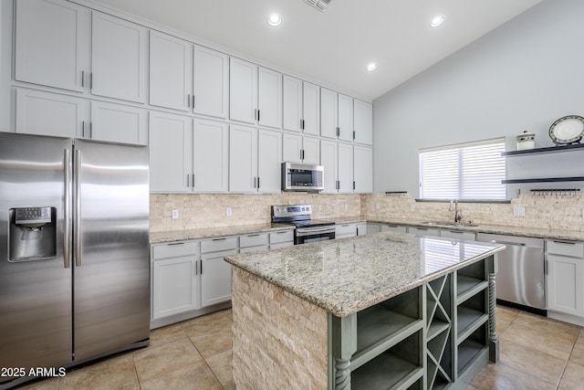 kitchen featuring sink, stainless steel appliances, light stone counters, white cabinets, and a kitchen island