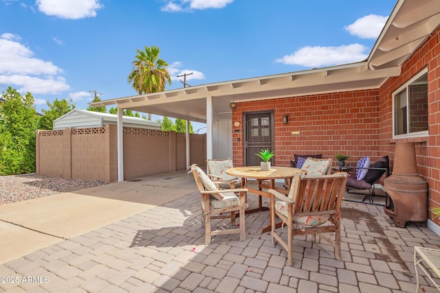 view of patio / terrace featuring an attached carport, driveway, outdoor dining area, and fence