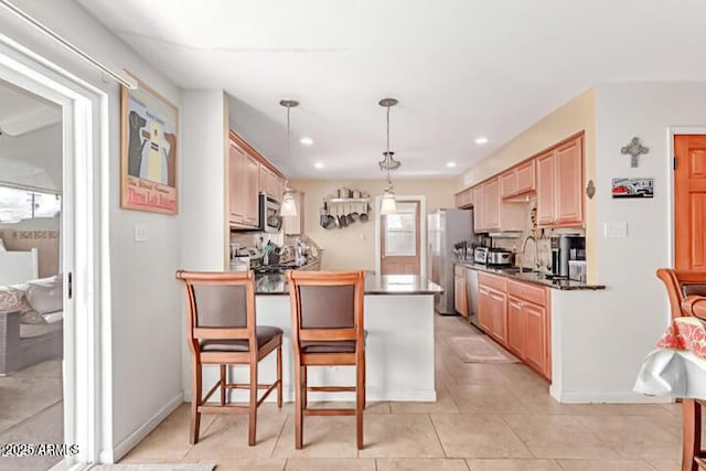 kitchen featuring dark countertops, a peninsula, a kitchen breakfast bar, stainless steel appliances, and a sink