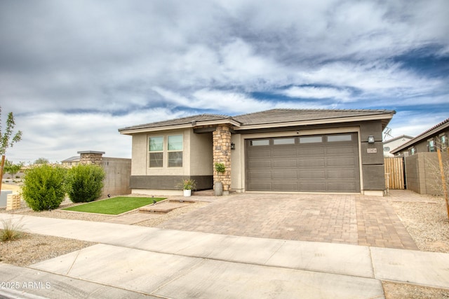 prairie-style home with an attached garage, fence, a tiled roof, decorative driveway, and stucco siding