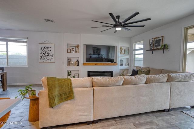 living area with plenty of natural light, visible vents, a ceiling fan, and a glass covered fireplace