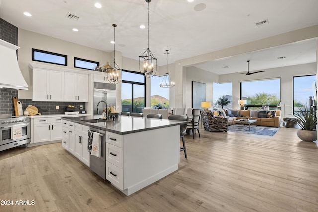 kitchen featuring decorative light fixtures, white cabinetry, ceiling fan with notable chandelier, high end appliances, and a kitchen island with sink