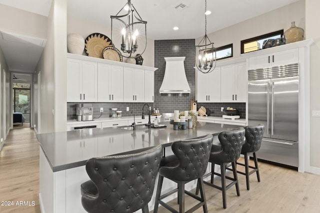 kitchen with white cabinets, built in refrigerator, a kitchen island with sink, and sink