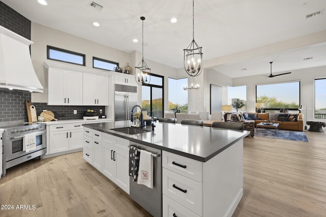 kitchen with custom exhaust hood, a center island with sink, high quality appliances, sink, and white cabinetry