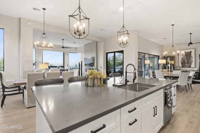 kitchen featuring sink, a center island with sink, white cabinetry, and pendant lighting