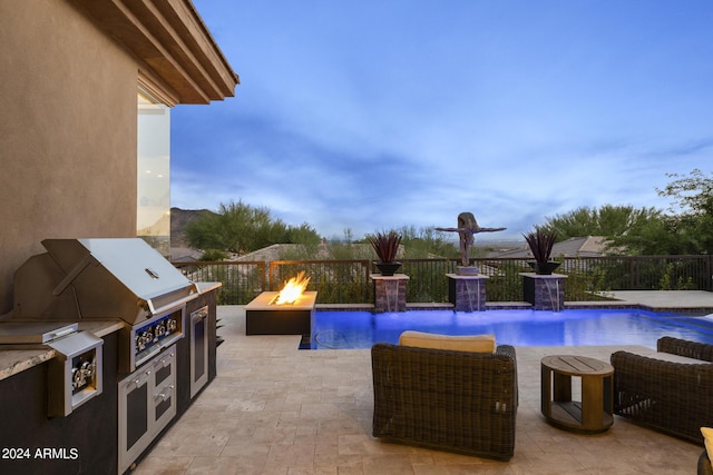 pool at dusk featuring an outdoor kitchen, pool water feature, an outdoor fire pit, and a patio