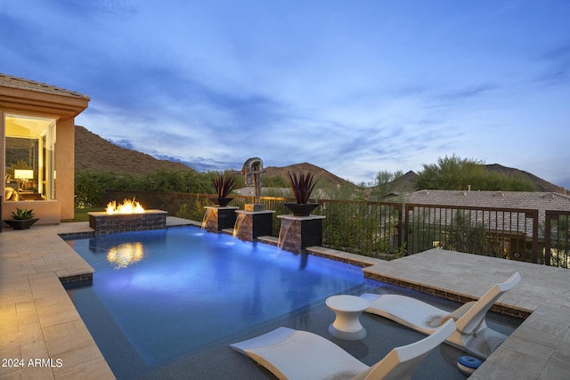 pool at dusk with an outdoor fire pit, a patio, pool water feature, and a mountain view