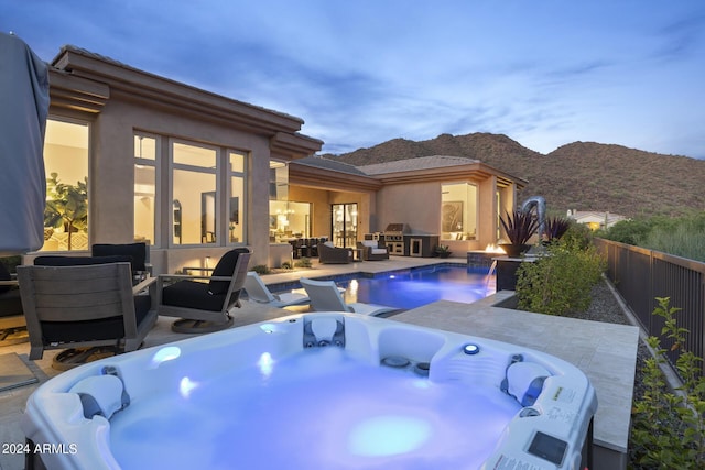 pool at dusk with an outdoor hangout area, a patio area, a mountain view, and a hot tub