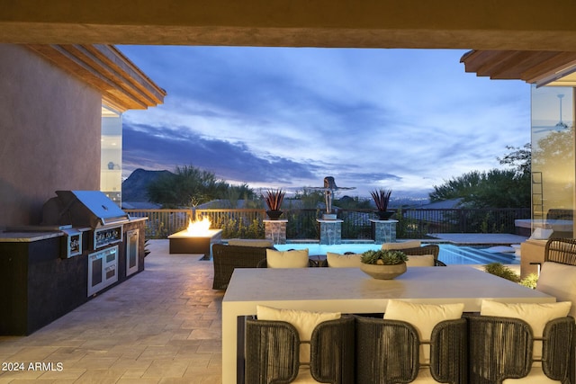 patio terrace at dusk featuring an outdoor fire pit, pool water feature, exterior kitchen, and a grill