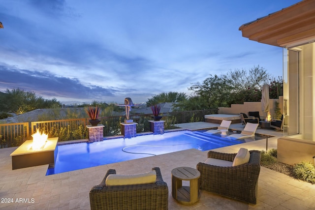 pool at dusk with an outdoor fire pit, pool water feature, a hot tub, and a patio