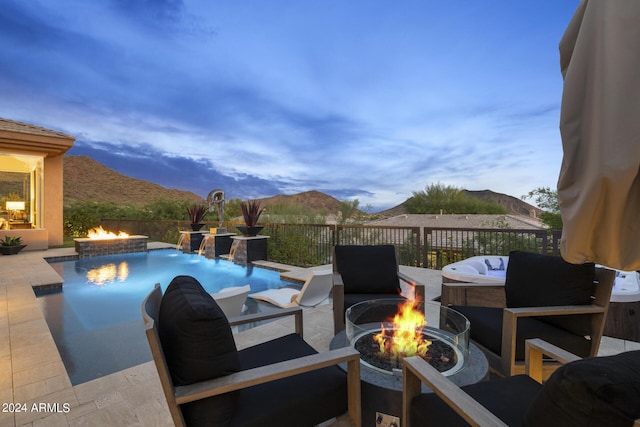 pool at dusk with a fire pit, pool water feature, a mountain view, and a patio area