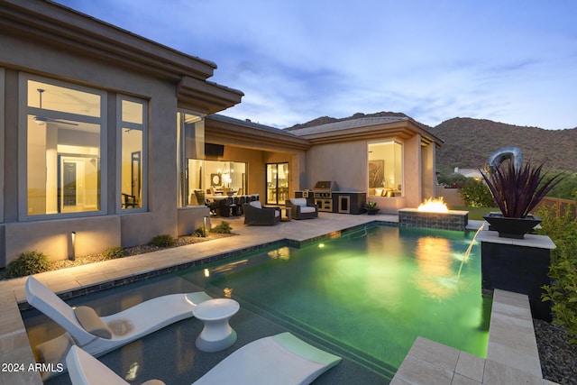 pool at dusk featuring an outdoor fire pit, a patio area, pool water feature, and area for grilling