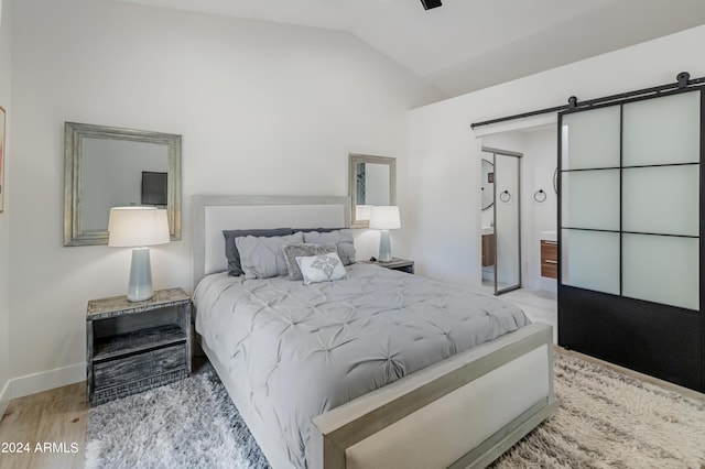 bedroom featuring vaulted ceiling, a barn door, and light hardwood / wood-style floors