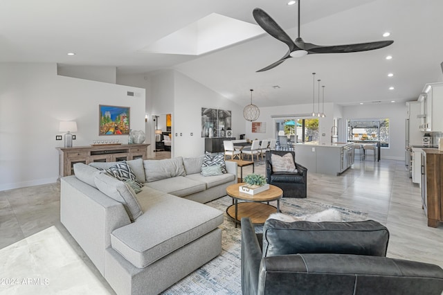 living room featuring ceiling fan, sink, and vaulted ceiling with skylight