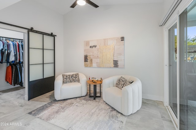 living area with ceiling fan, vaulted ceiling, and a barn door