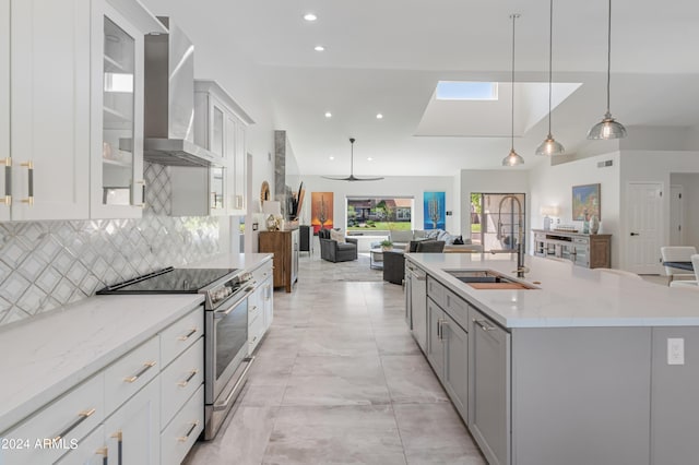 kitchen featuring light stone countertops, hanging light fixtures, a center island with sink, wall chimney range hood, and electric range