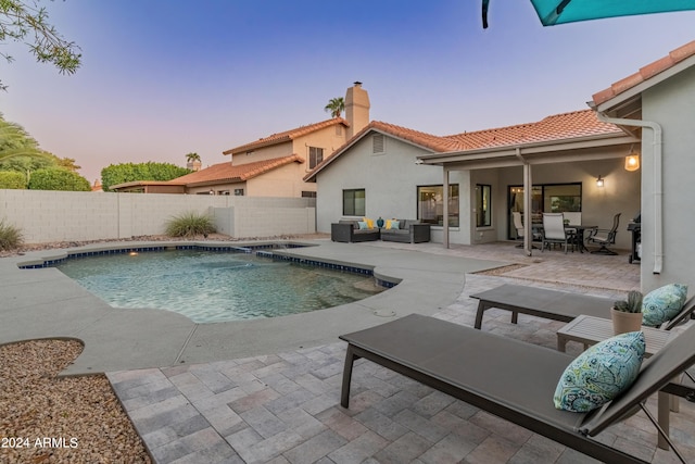 pool at dusk with pool water feature, an outdoor hangout area, and a patio