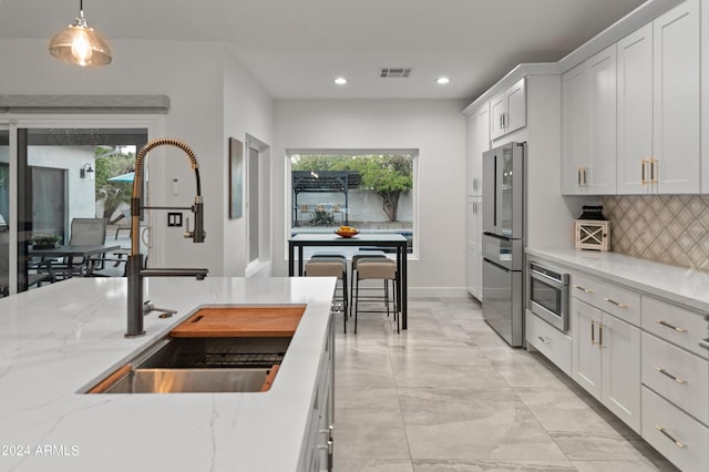 kitchen with sink, white cabinetry, backsplash, and hanging light fixtures