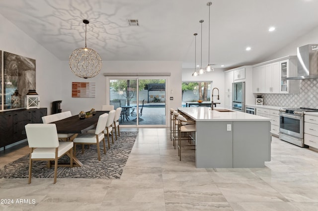 kitchen featuring white cabinets, stainless steel appliances, decorative light fixtures, and a center island with sink