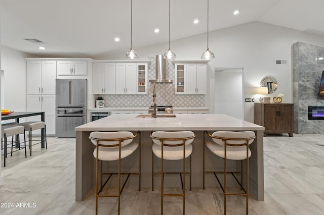 kitchen featuring stainless steel appliances, white cabinetry, wall chimney exhaust hood, lofted ceiling, and a kitchen breakfast bar