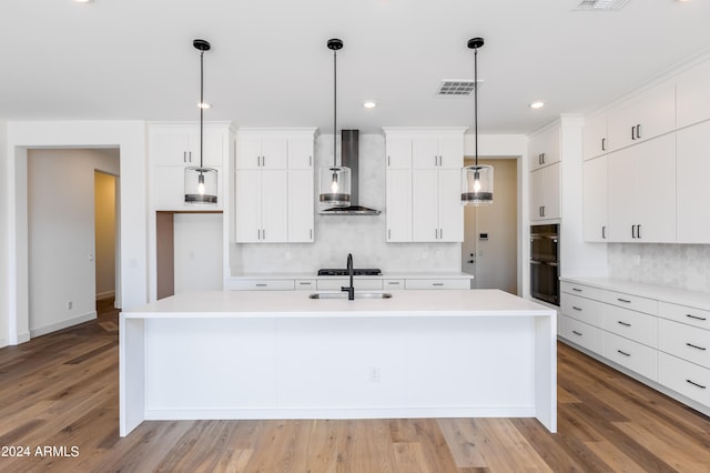 kitchen featuring white cabinets, hardwood / wood-style flooring, a center island with sink, and wall chimney exhaust hood