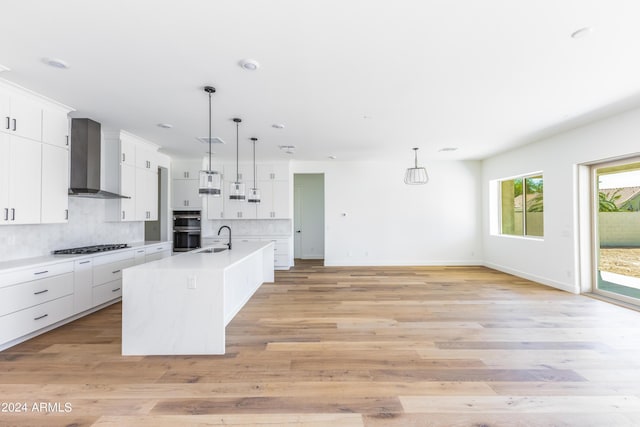 kitchen with wall chimney range hood, decorative backsplash, stainless steel double oven, white cabinets, and a sink