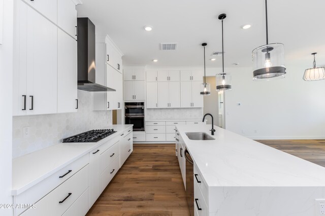 kitchen with hanging light fixtures, wall chimney range hood, white cabinets, and a kitchen island with sink