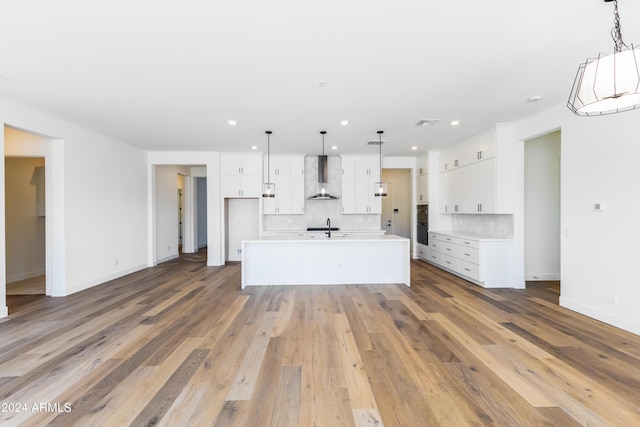 kitchen featuring decorative backsplash, wall chimney range hood, light wood finished floors, and white cabinets