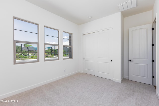 unfurnished bedroom featuring visible vents, baseboards, light colored carpet, and a closet