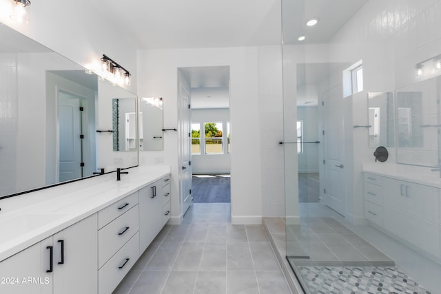 bathroom featuring tile patterned flooring, baseboards, walk in shower, double vanity, and a sink