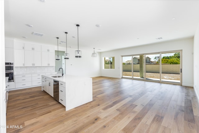 kitchen with white cabinets, light hardwood / wood-style flooring, appliances with stainless steel finishes, decorative backsplash, and a kitchen island with sink