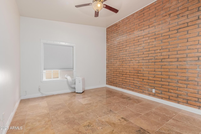 spare room with baseboards, a ceiling fan, and brick wall