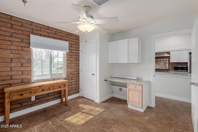 unfurnished office featuring ceiling fan, built in study area, brick wall, stone finish floor, and baseboards