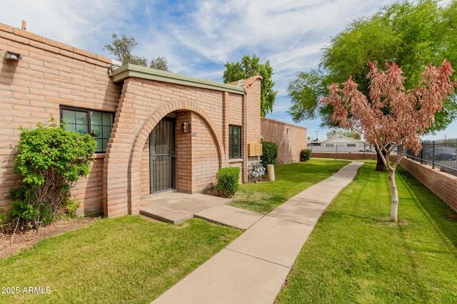 doorway to property with brick siding, a lawn, and fence