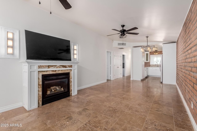 unfurnished living room featuring visible vents, a glass covered fireplace, brick wall, stone finish flooring, and ceiling fan with notable chandelier