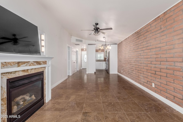 unfurnished living room with baseboards, ceiling fan with notable chandelier, and brick wall