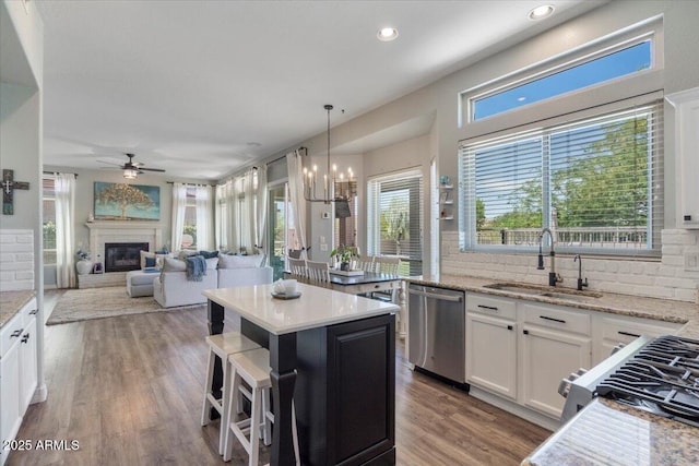 kitchen featuring a kitchen island, backsplash, a sink, ceiling fan with notable chandelier, and stainless steel appliances