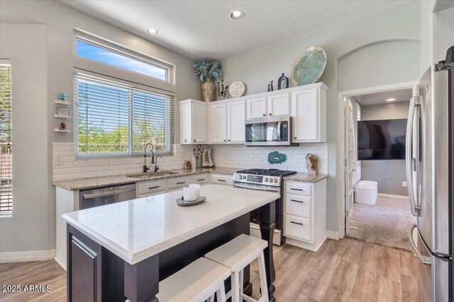 kitchen with decorative backsplash, white cabinets, a sink, light wood finished floors, and stainless steel appliances