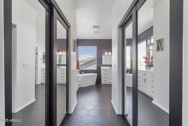 hall featuring dark tile patterned floors, baseboards, and visible vents
